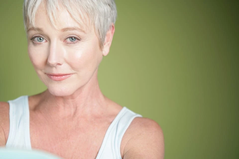 Hydrafacial_banner_image_2 Mature woman with short hair in front of a green solid background.